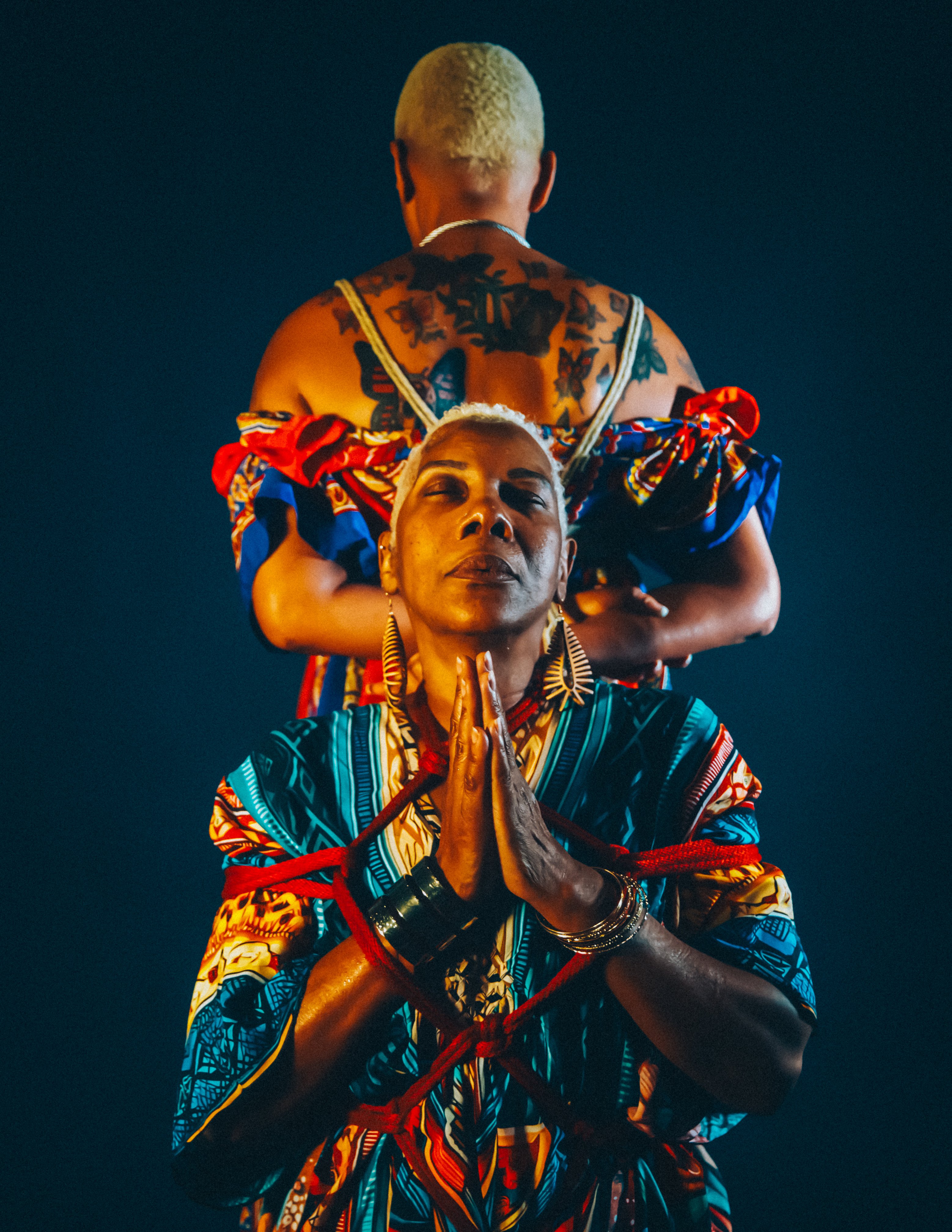 A figure held in rope, light catching the shoulders and clavicle.