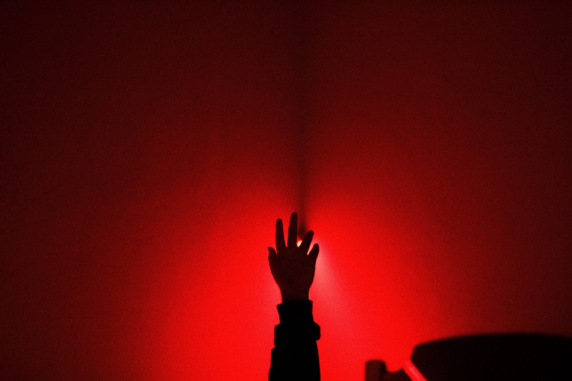 Mood still: a red-lit hand raised in shadow.