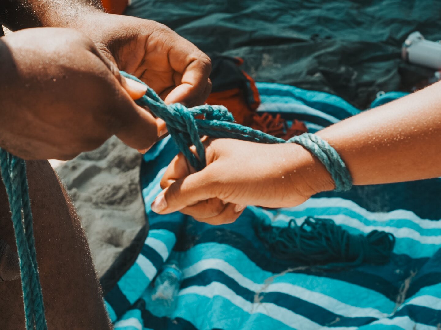 Hands and rope, mid-tie, sand on the fingers.