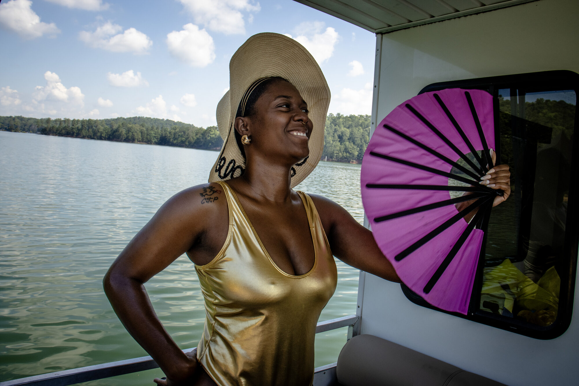 A woman laughs with a fan on the deck, lake behind her