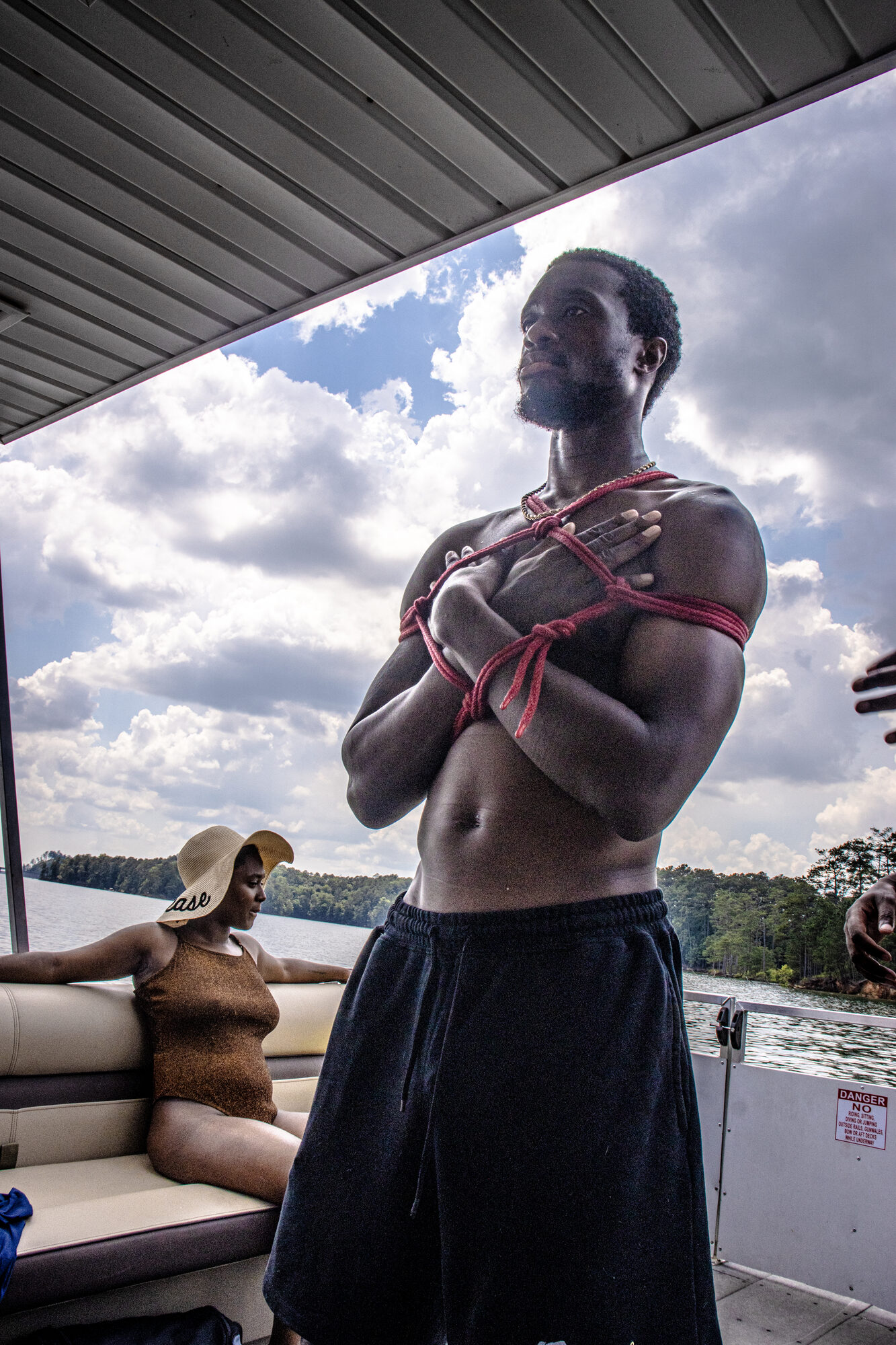 A man stands with arms crossed over a rope chest harness, looking out across the lake