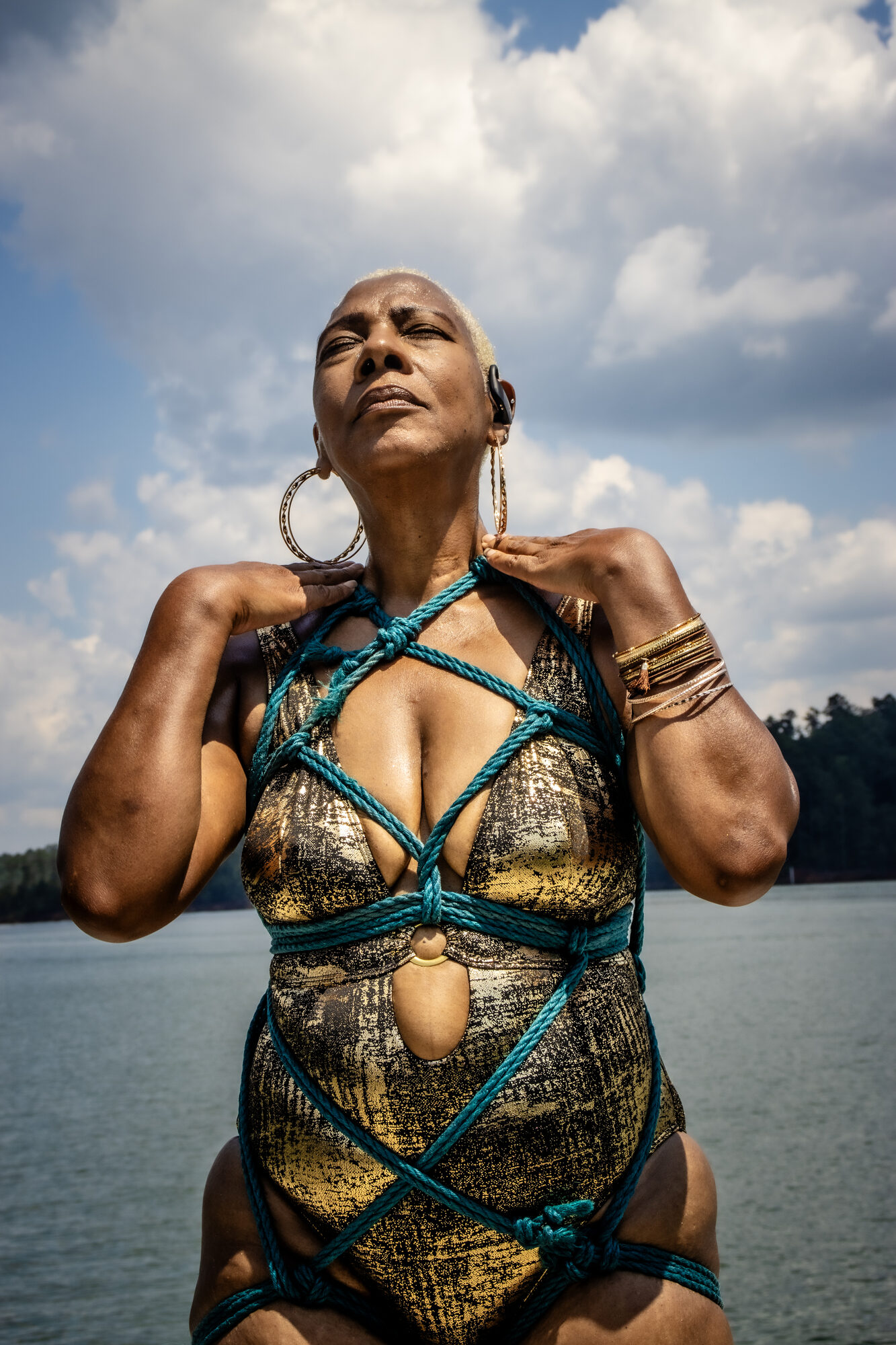 A woman lifts her face to the open sky, rope across a gold suit