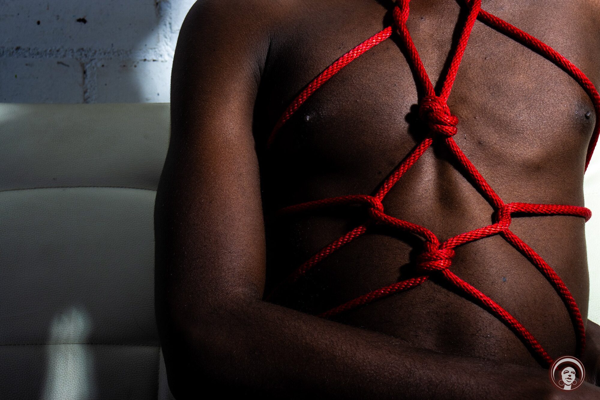 Red rope harness laid across a bare chest in close detail